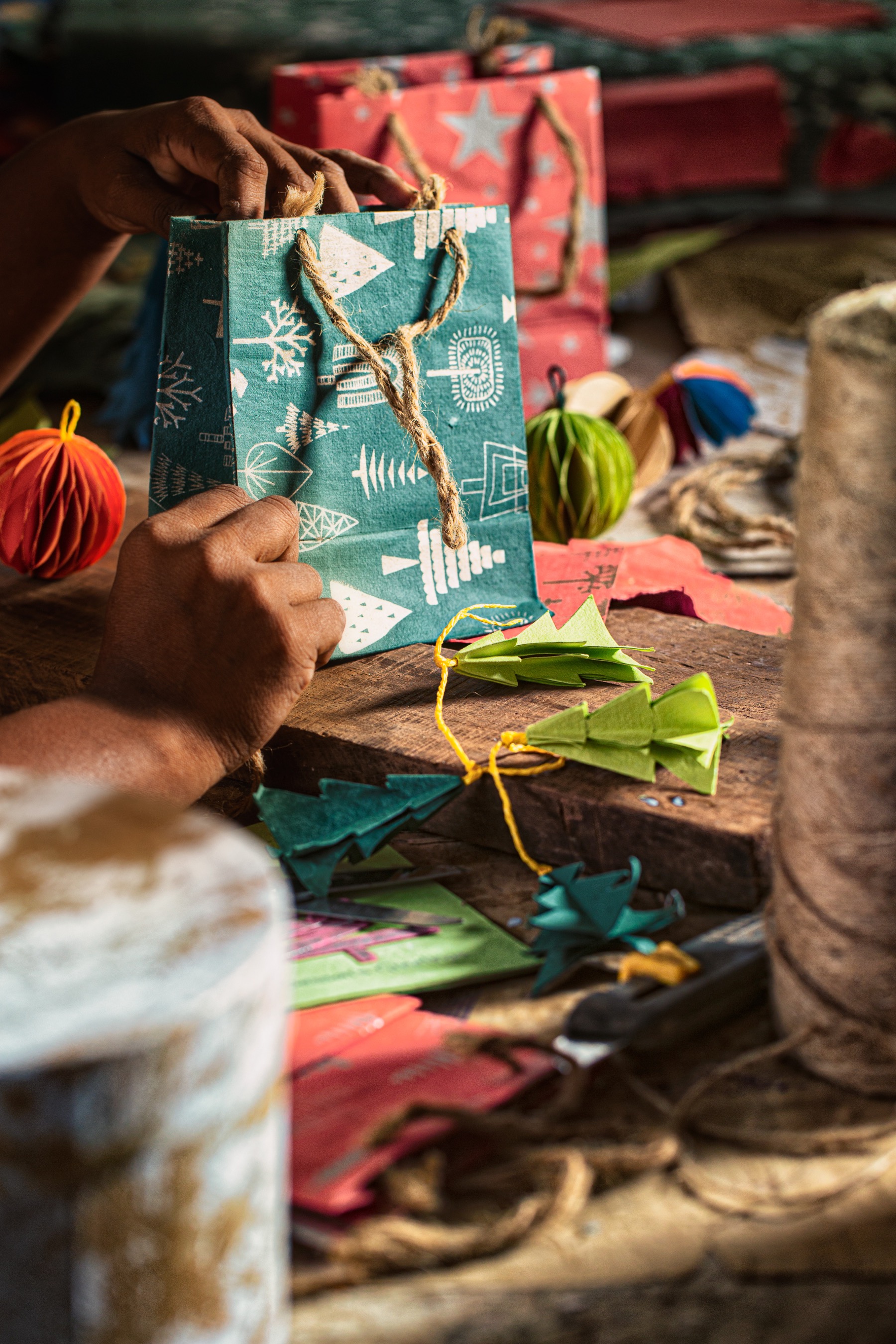 Hands assembling a green patterned handmade paper gift bag with rope handles