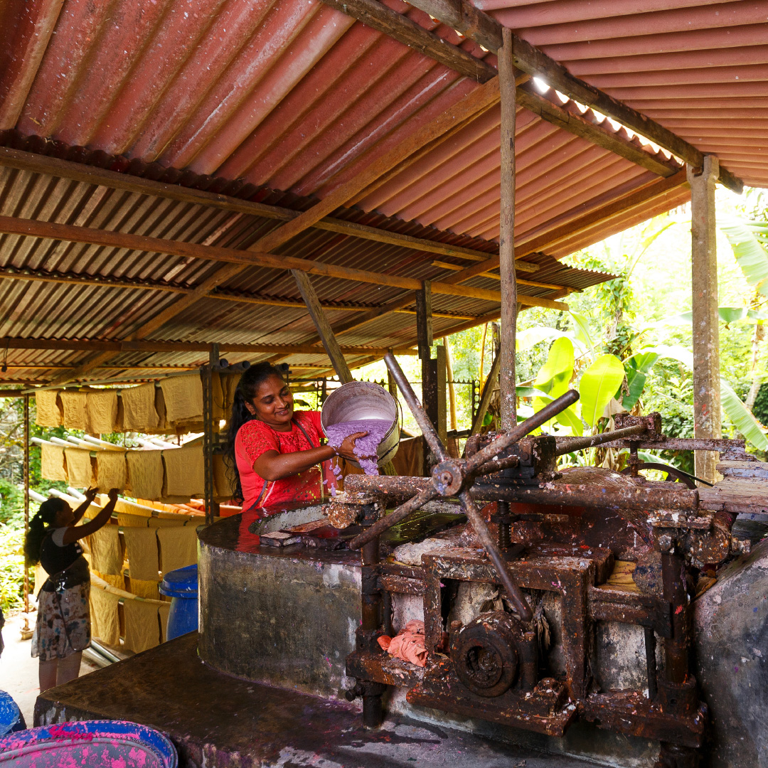 A woman pouring pulp at the manual paper machine under the open workshop roof