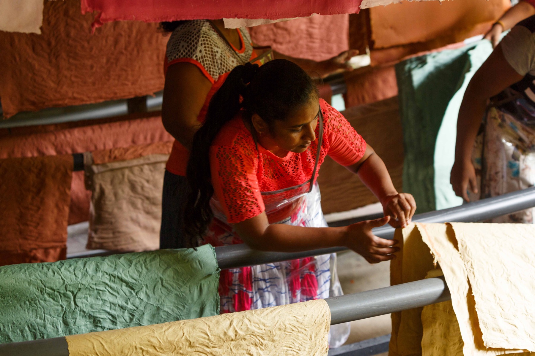 A woman checking sheets of colourful handmade paper drying on racks