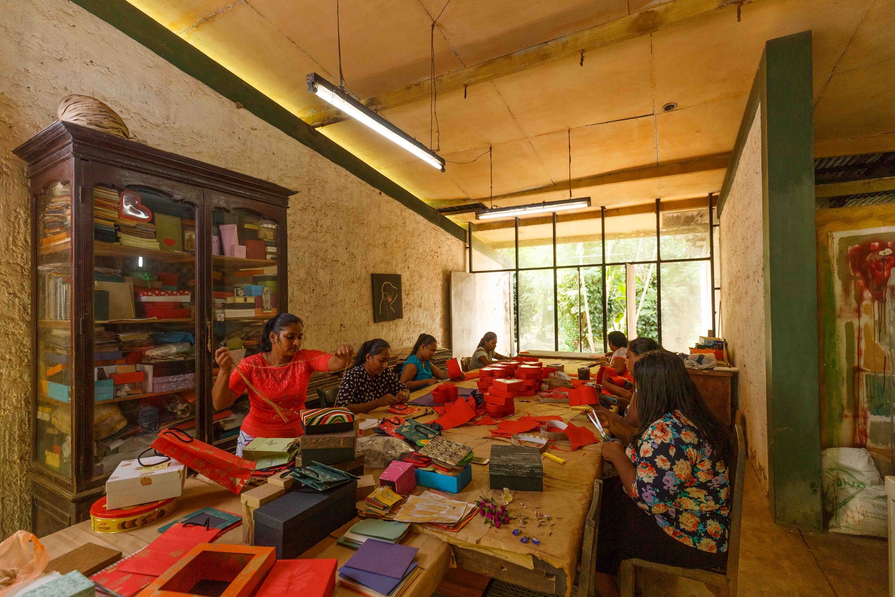 Women crafting colourful paper products around a large wooden table in the Kadadasi workshop